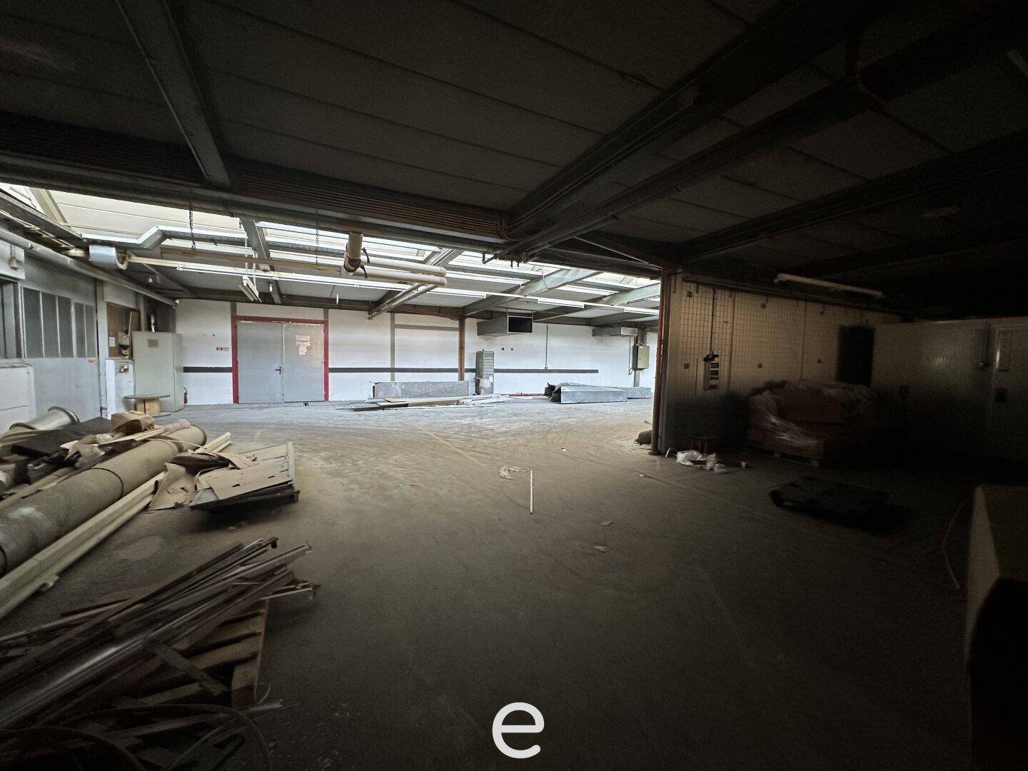 Dunklerer Bereich der Lagerhalle mit sichtbaren Stahlträgern und gelagerten Materialien, der Renovierungsbedarf hat.