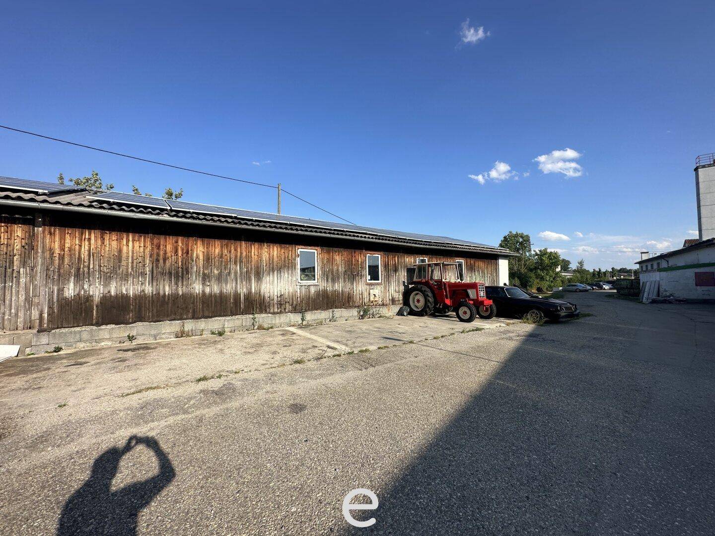 Rustikales Holzgebäude mit einem geparkten Traktor und Solarpaneelen auf dem Dach, das Renovierungsbedarf zeigt.