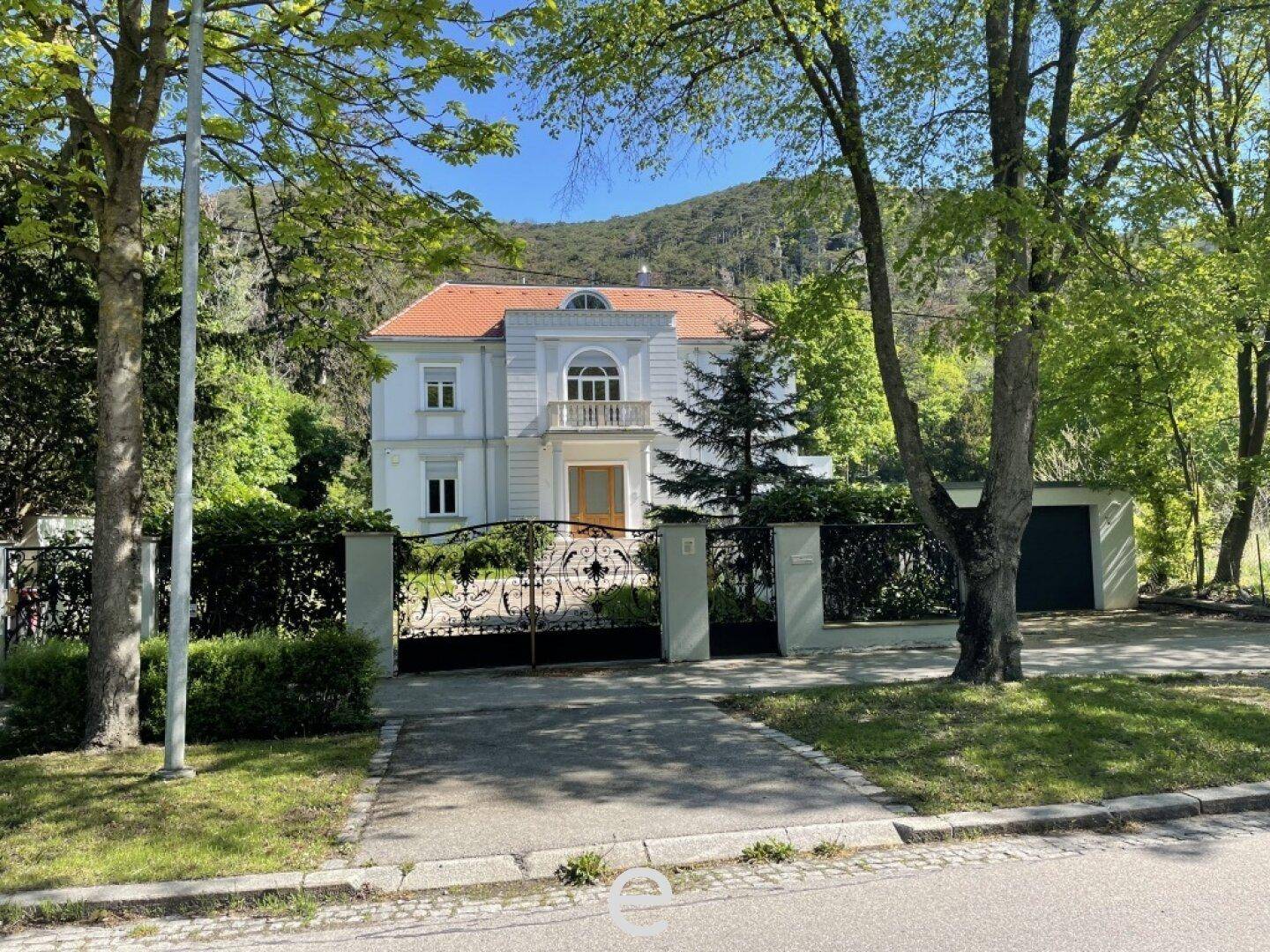 Die Villa von der Straße aus gesehen, umgeben von Bäumen und einem schmiedeeisernen Tor.