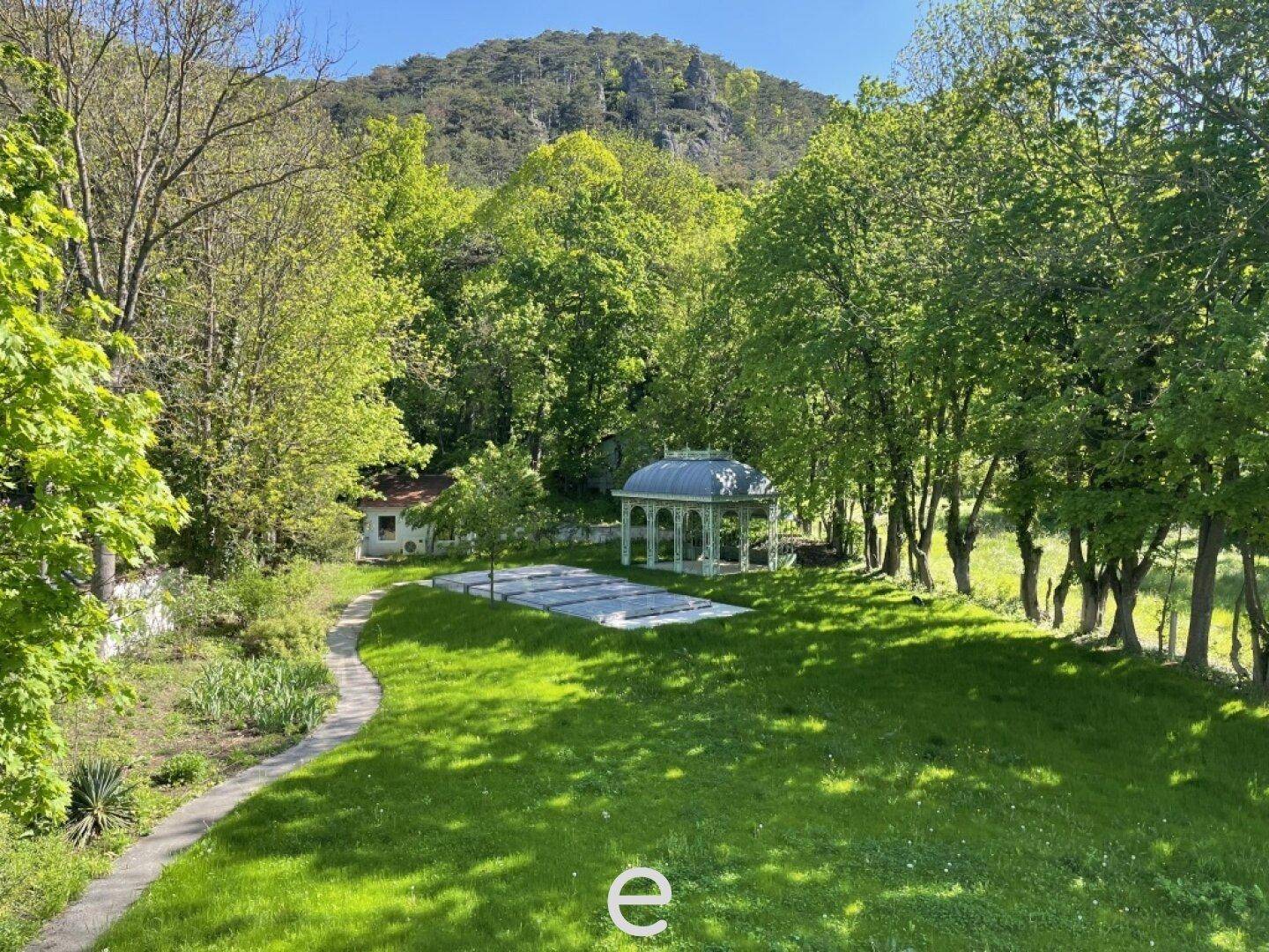 Weitläufiger Garten mit gepflegtem Rasen, altem Baumbestand und einem eleganten Pavillon.