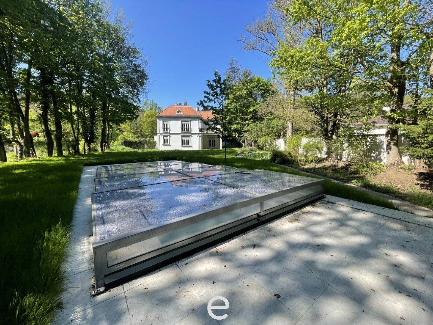 Großer Gartenbereich mit überdachtem Pool und Blick auf die historische Villa.