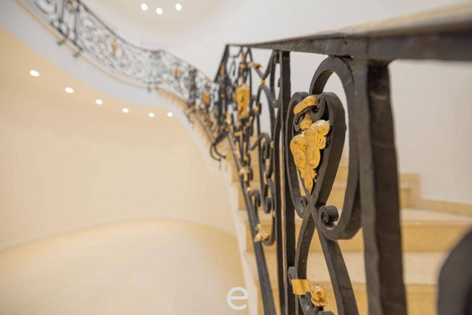 Detailaufnahme des kunstvollen schmiedeeisernen Treppengeländers mit goldenen Akzenten.