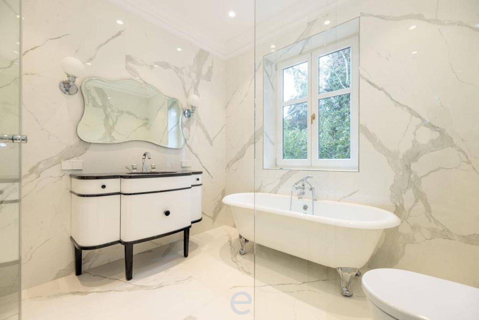 Luxuriöses Badezimmer mit freistehender Badewanne, Marmorfliesen und Fenster.
