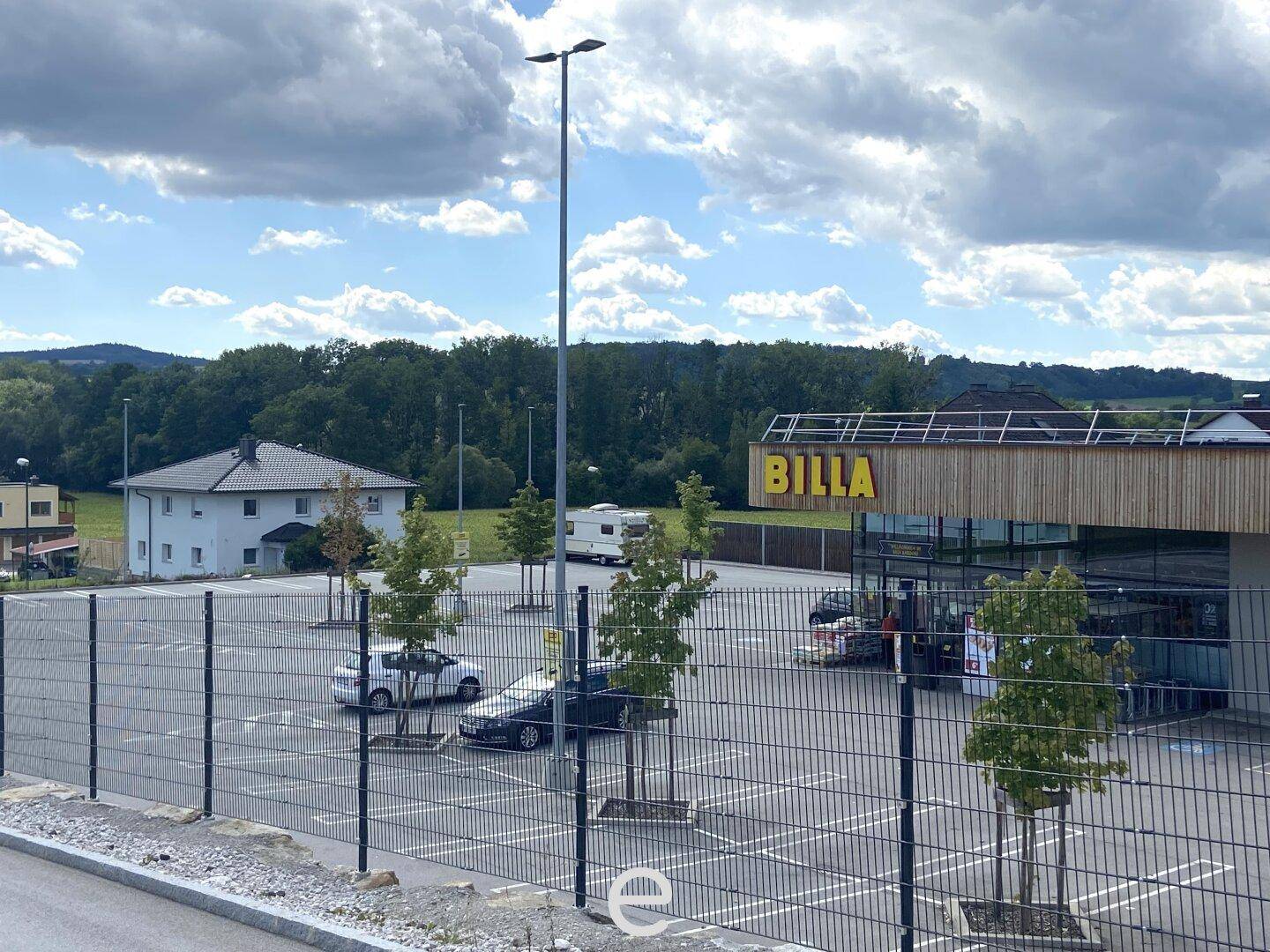 Supermarkt mit großem Parkplatz und ländlicher Umgebung unter einem teilweise bewölkten Himmel.