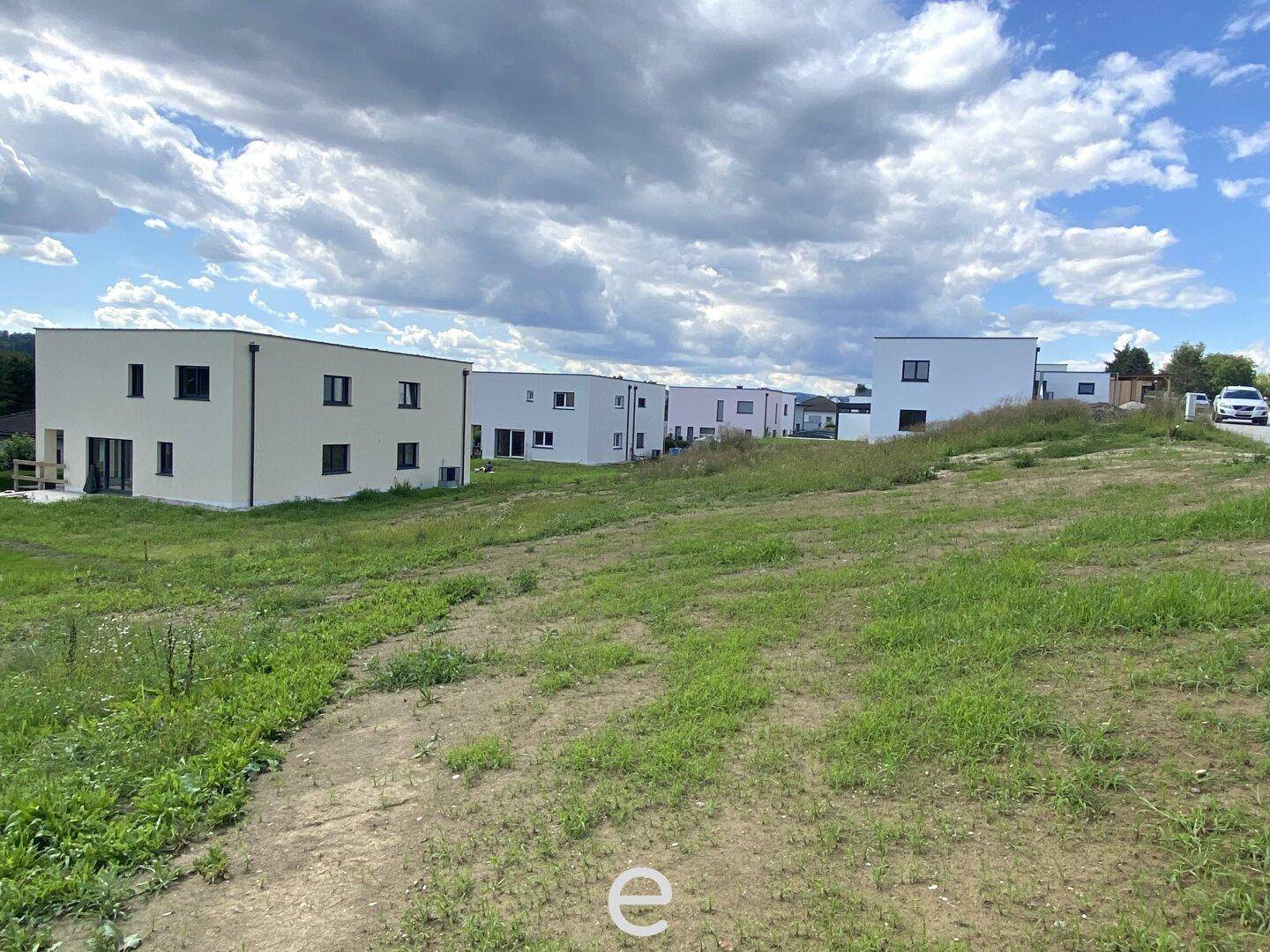 Moderne Neubauten auf einem weitläufigen Grundstück mit grüner Wiese unter bewölktem Himmel.