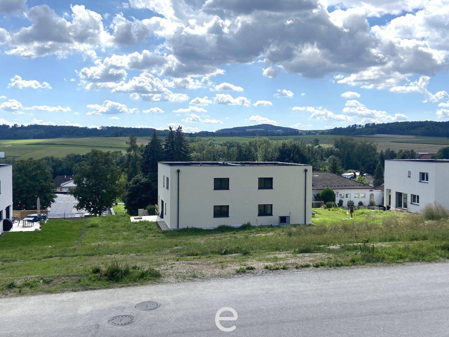 Modernes Gebäude mit Blick auf weite Felder und bewaldete Hügel unter einem bewölkten Himmel.