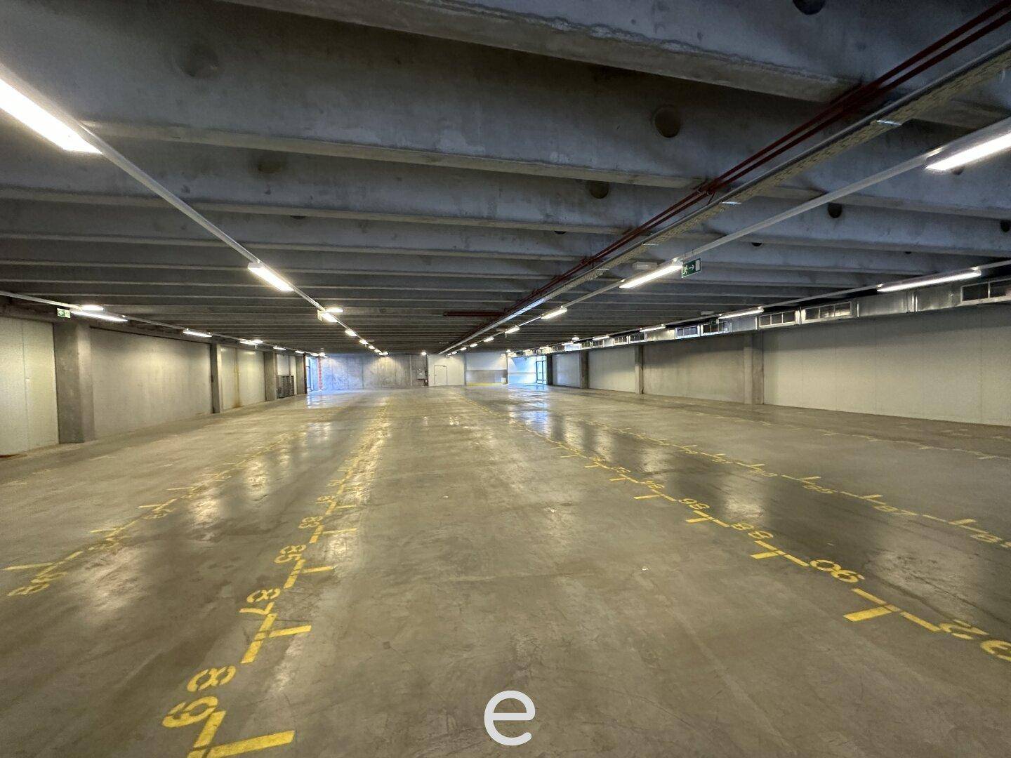 Große, leere Tiefgarage mit Betonboden und durchgehenden Leuchtstoffröhren.