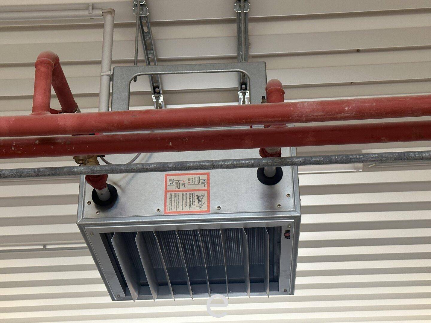 Industrielle Heiz- oder Lüftungsanlage mit roten Rohren an der Decke eines Lagerraums.