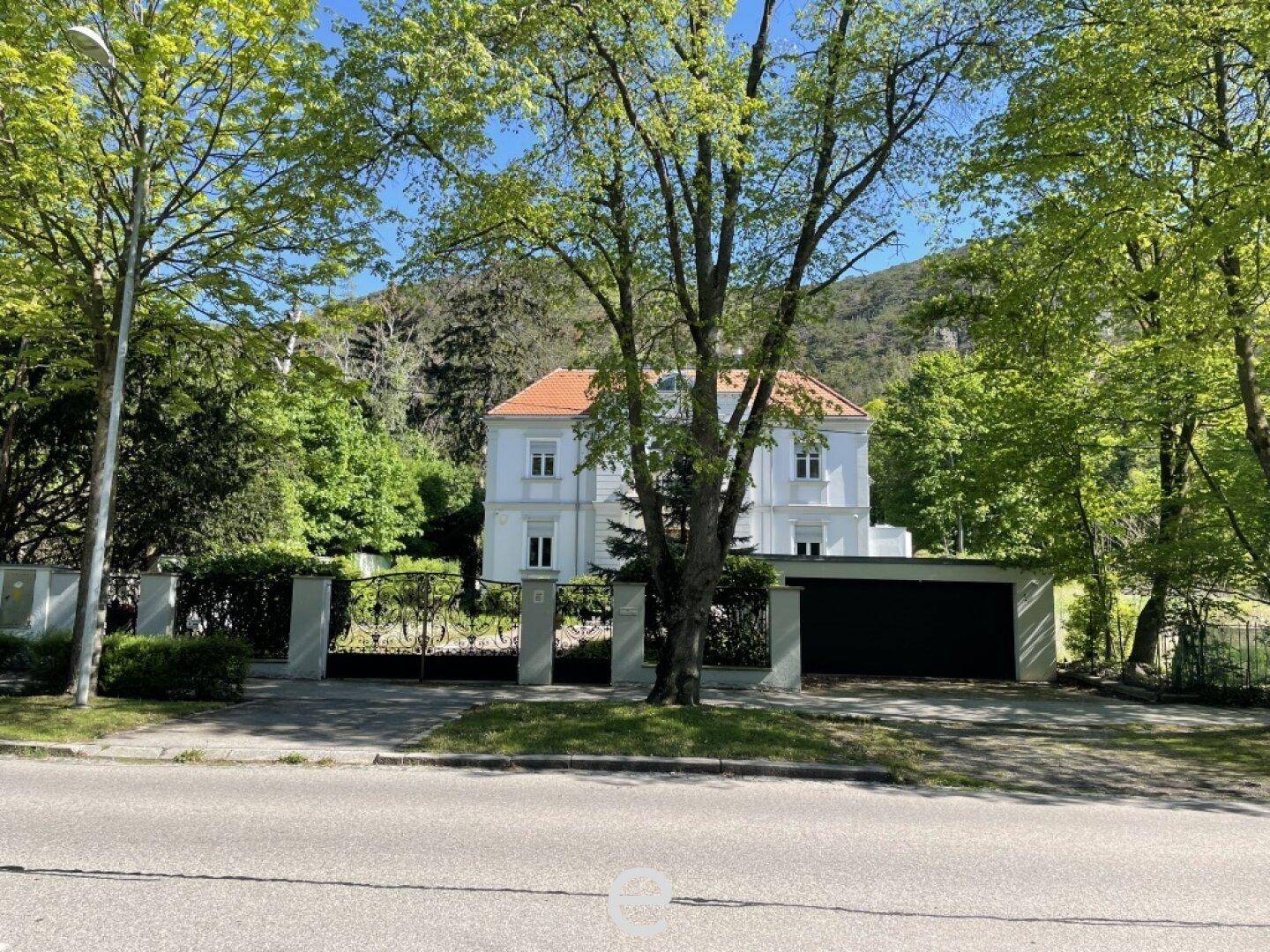 Die Villa von der Straße aus gesehen, umgeben von Bäumen und einem schmiedeeisernen Tor.