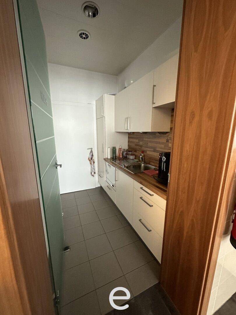 Schmale, funktionale Küche mit weißen Schränken, Holzarbeitsplatte und gefliestem Boden.