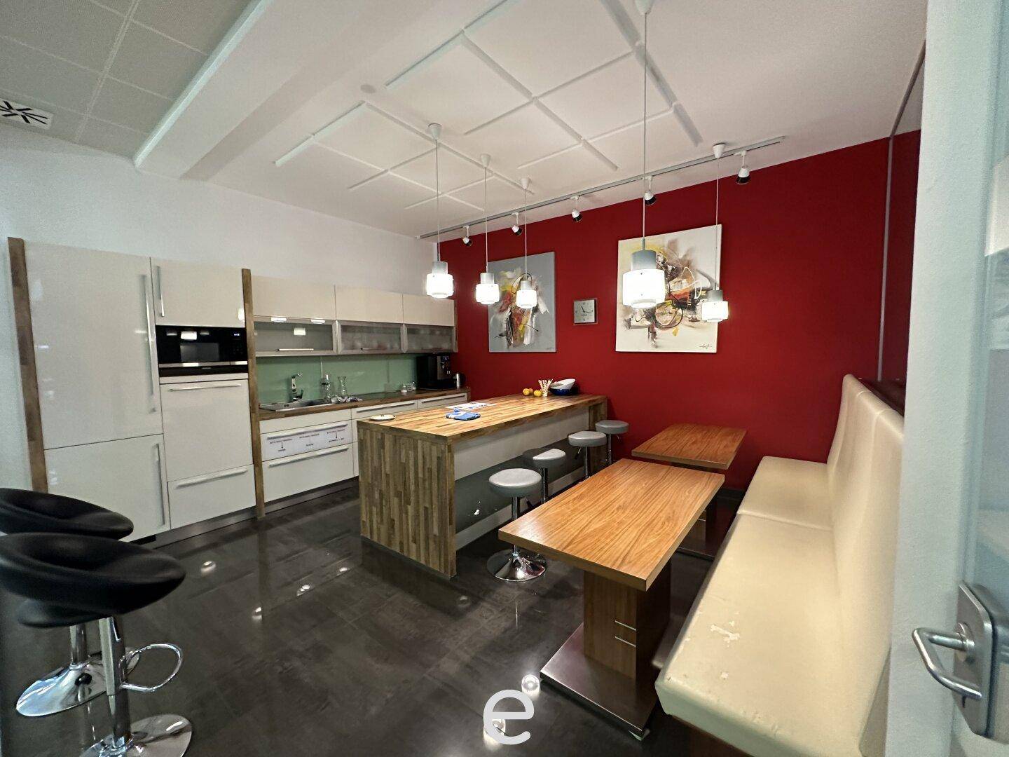 Moderne offene Küche mit Kücheninsel, Holzelementen und roter Akzentwand, ideal für geselliges Beisammensein.