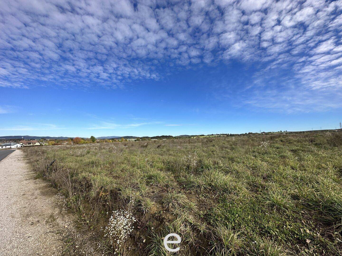 Weitläufiges, unbebautes Grundstück mit Gras und Büschen unter einem klaren blauen Himmel.