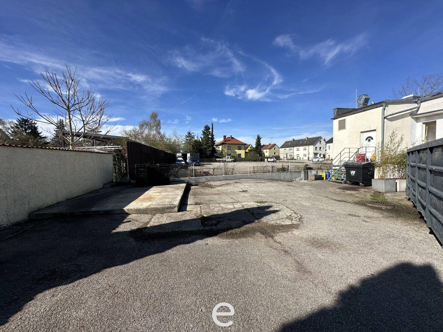 Großer, unbefestigter Parkplatz mit umliegenden Gebäuden unter einem weiten blauen Himmel.