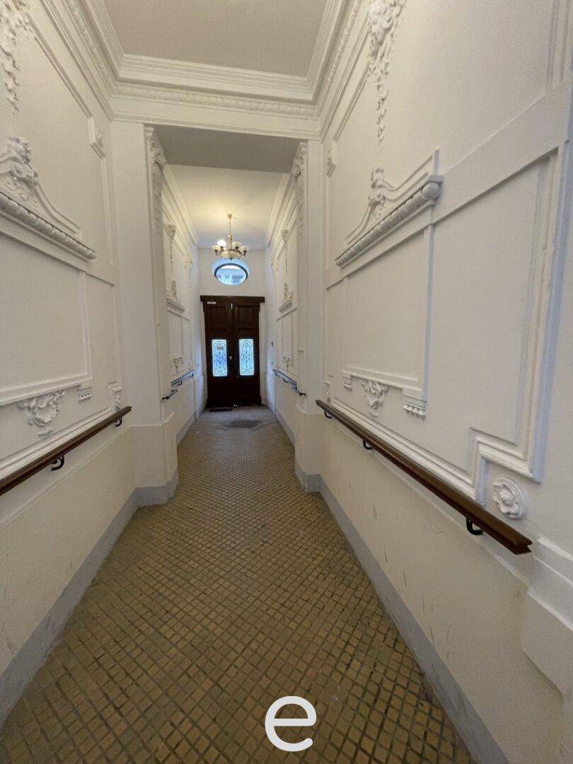 Langer Flur mit dekorativen Wandpaneelen, Stuckelementen und gemustertem Fliesenboden in einem Altbau.