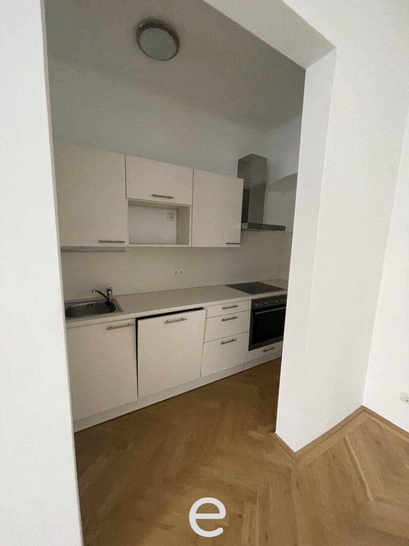 Kleine, funktionale Küchenzeile mit weißen Schränken, Spüle und Kochfeld in einem schmalen Raum.