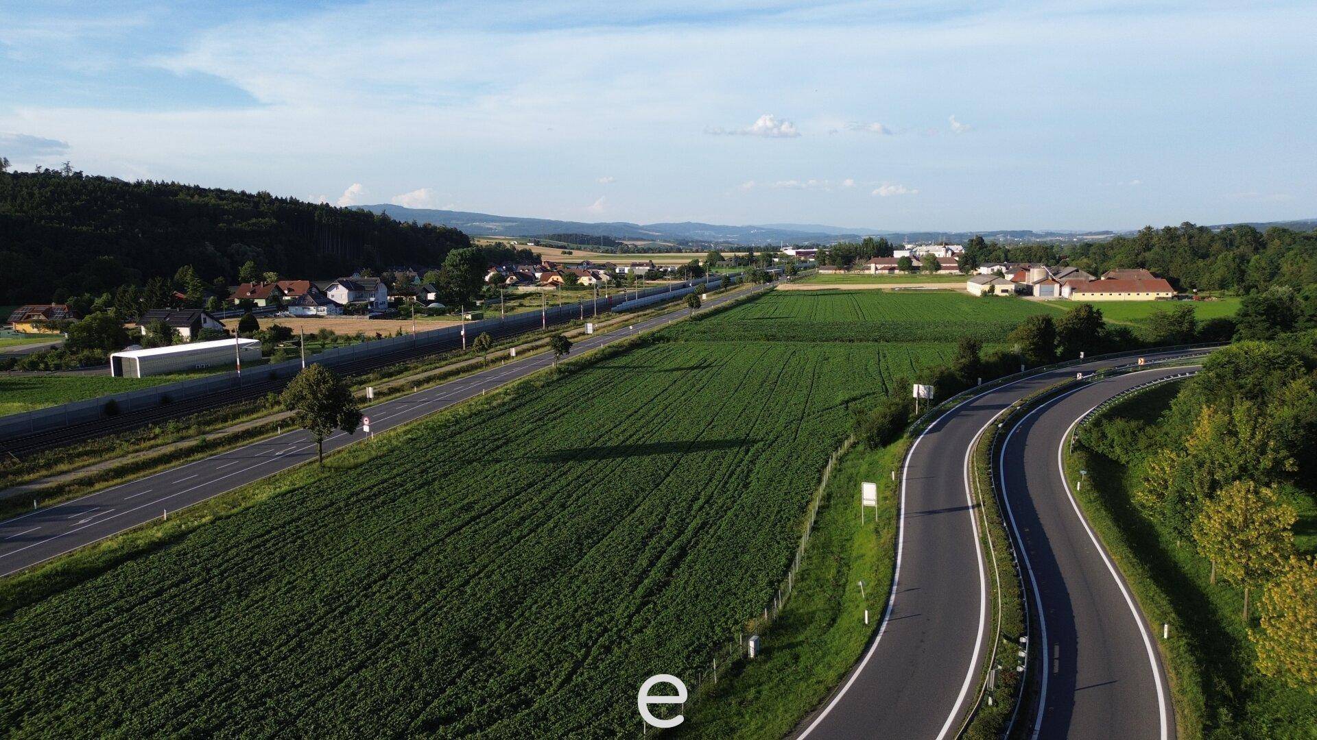 Panoramablick aus der Luft auf eine Autobahn, grüne Felder und ein kleines Dorf am Horizont.