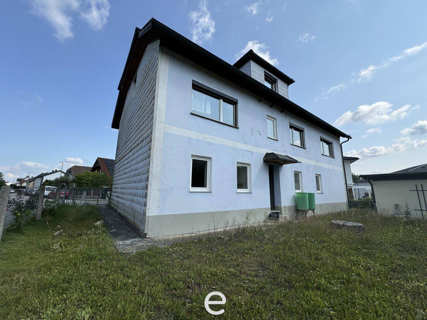 Blau gestrichenes Haus mit Schindelfassade und mehreren Fenstern unter einem klaren Himmel.