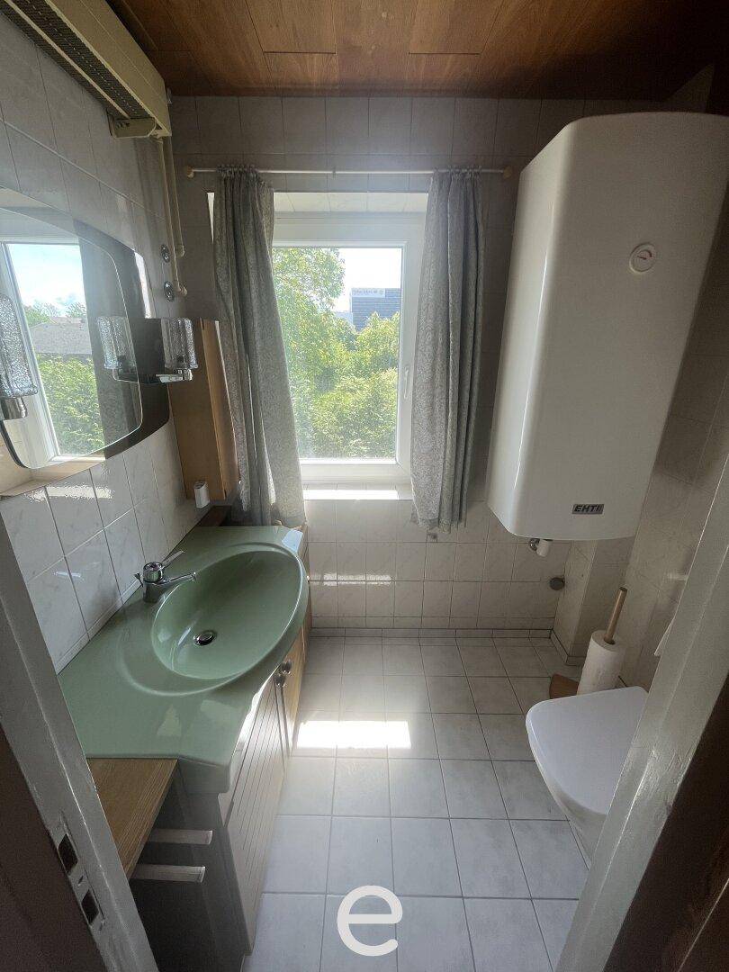 Helles Badezimmer mit grünem Waschbecken, Fenster und weißem Boiler an der Wand.