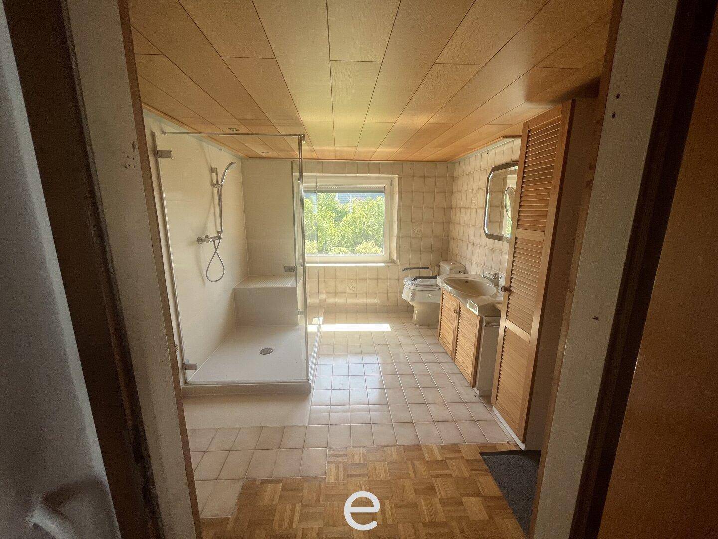 Badezimmer mit Holzdecke, Fliesenboden und einer modernen Duschkabine mit Fenster.