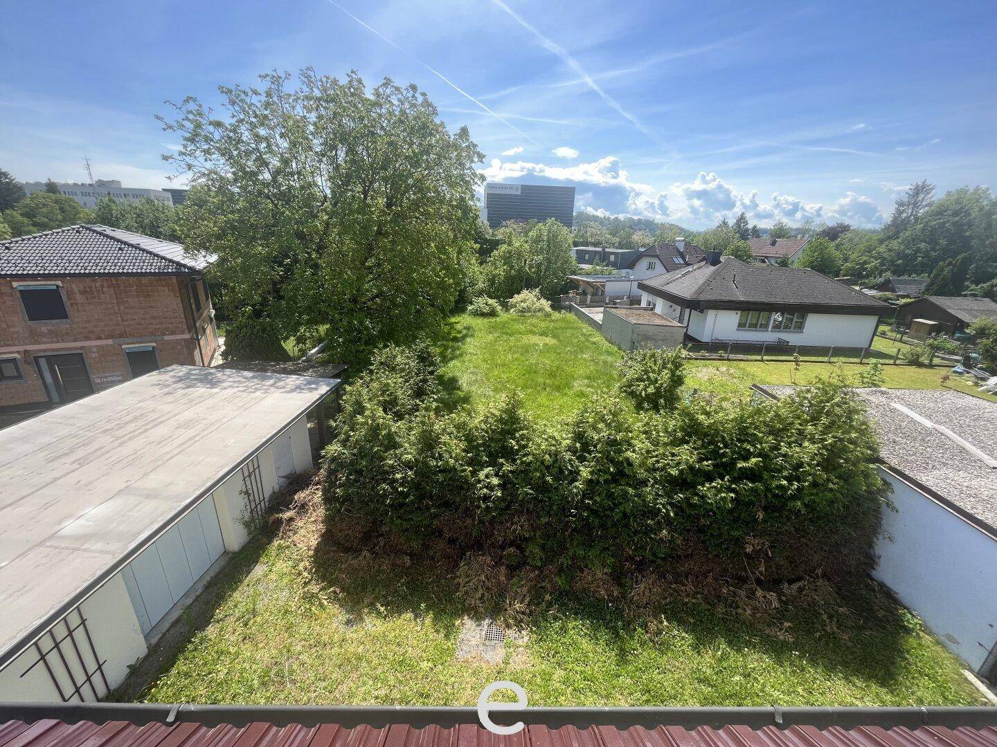 Überblick über das Grundstück mit umliegenden Häusern und viel Grün unter strahlend blauem Himmel.
