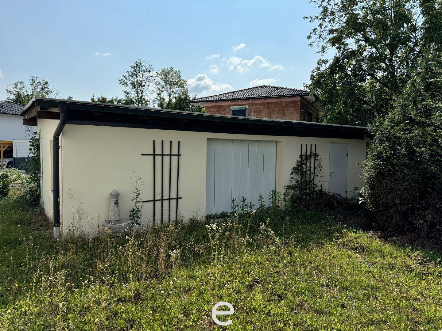 Freistehende Garage oder Nebengebäude mit weißer Fassade und grünem Gras im Vordergrund.