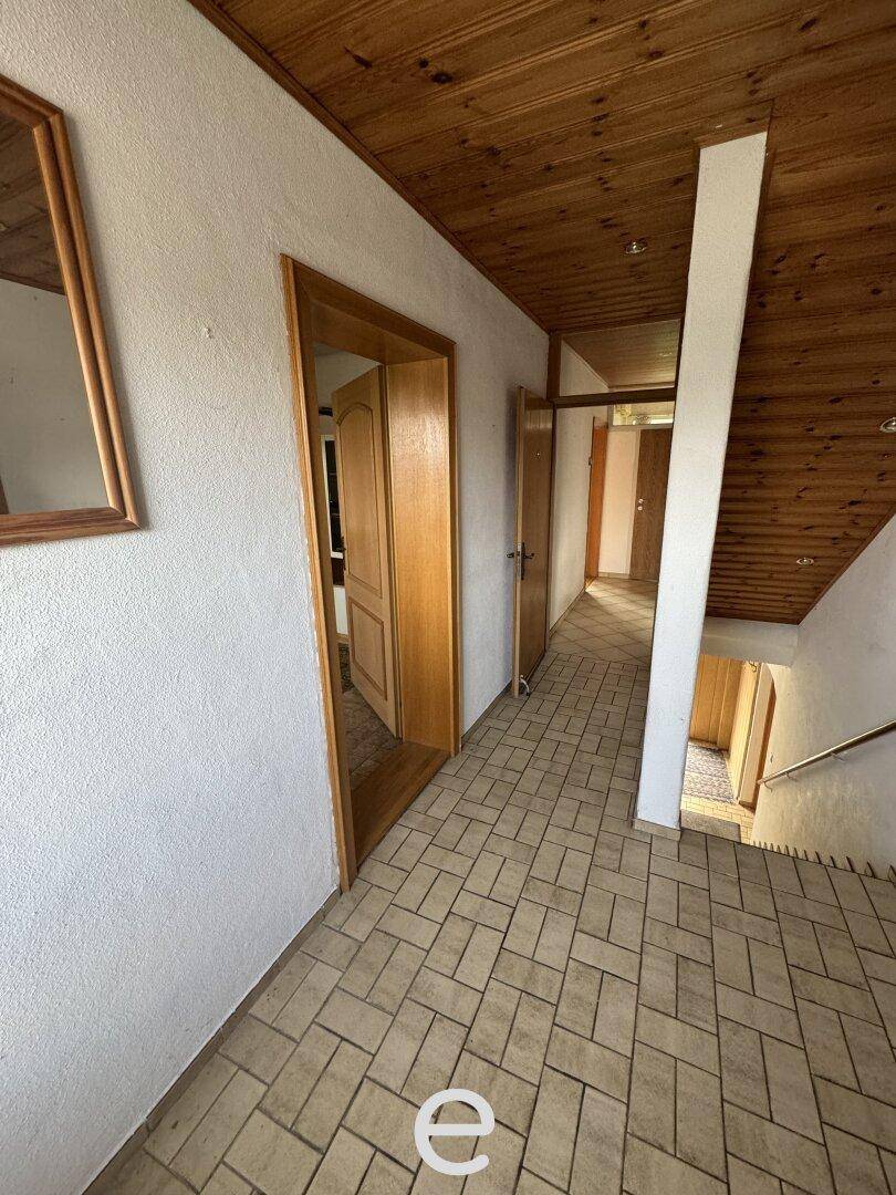 Flur mit Holzdecke, Fliesenboden und mehreren Holztüren, die zu anderen Räumen führen.