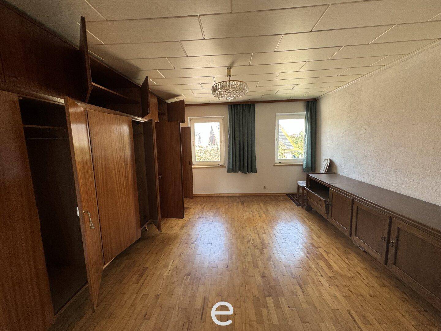Geräumiges Schlafzimmer mit Holzboden, großen Kleiderschränken und zwei Fenstern.