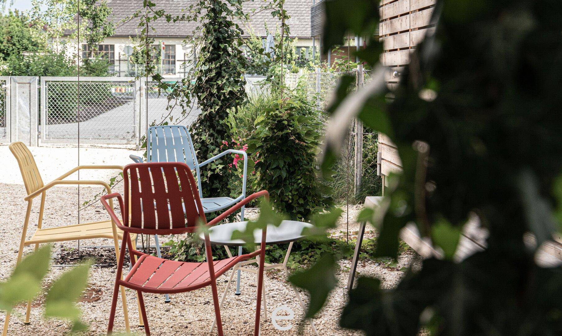 Farbenfrohe Gartenstühle in einem begrünten Außenbereich der Wohnanlage.
