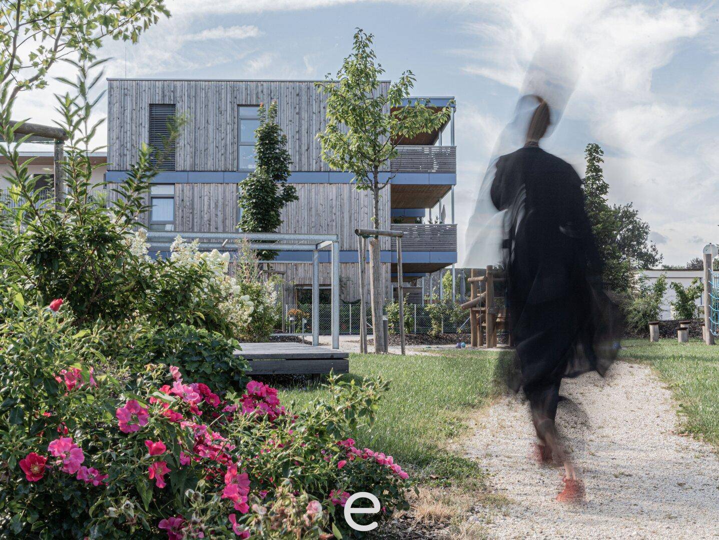 Blühender Gartenbereich mit Spazierweg und moderner Holzfassade im Hintergrund.