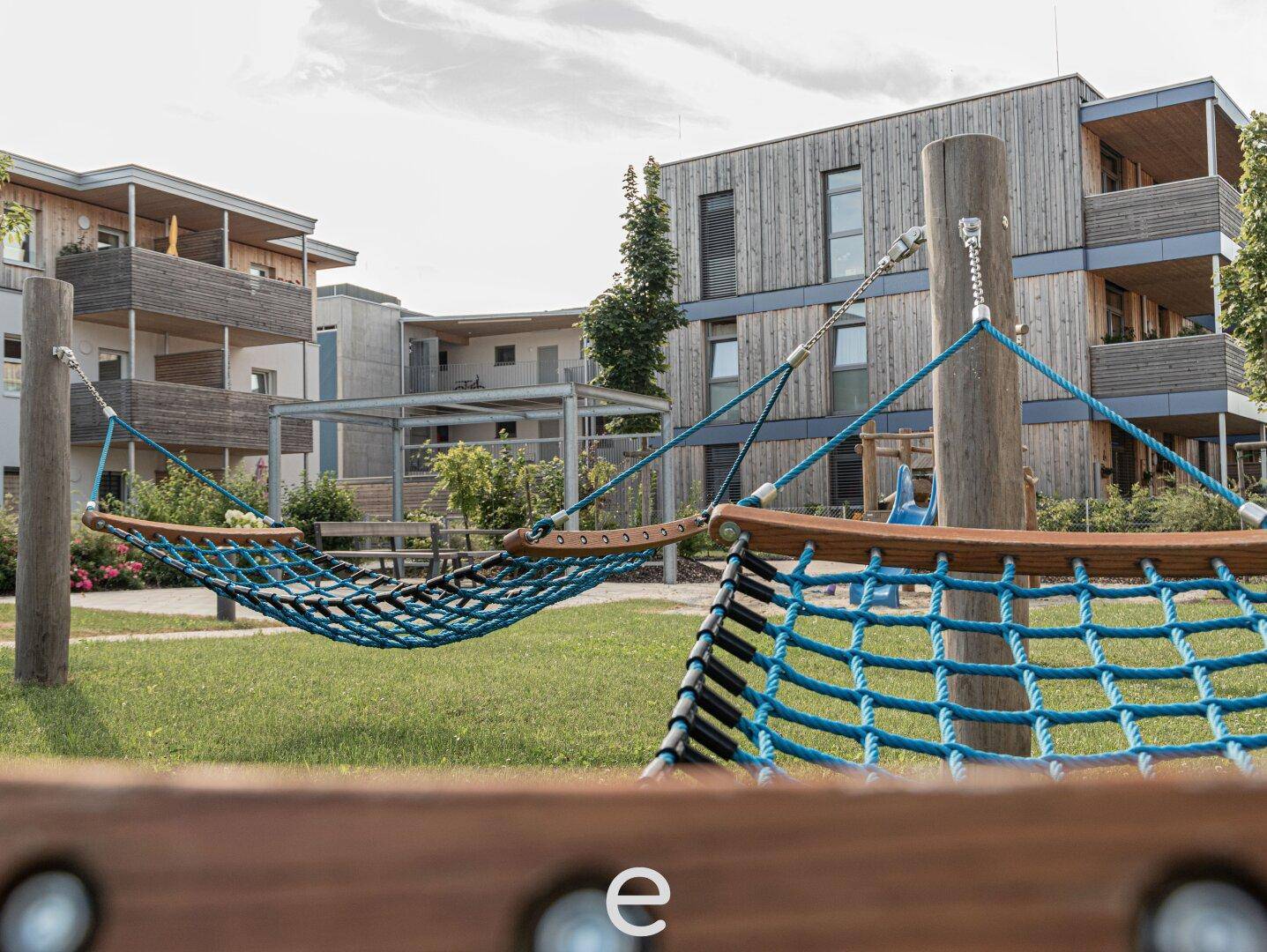 Entspannungsbereich im Gemeinschaftsgarten mit Hängematten und moderner Architektur.