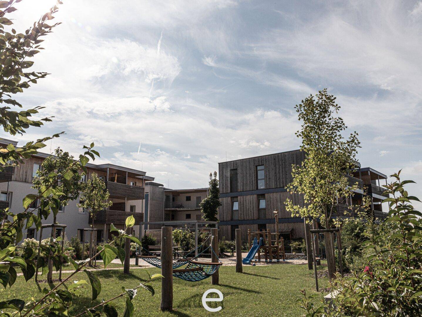 Weitläufiger Gemeinschaftsgarten mit Spielplatz und modernen Wohngebäuden unter einem bewölkten Himmel.