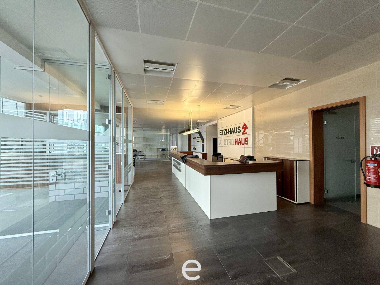 Langer, moderner Empfangsbereich mit Glaswänden, dunklem Fliesenboden und einer eleganten Theke.