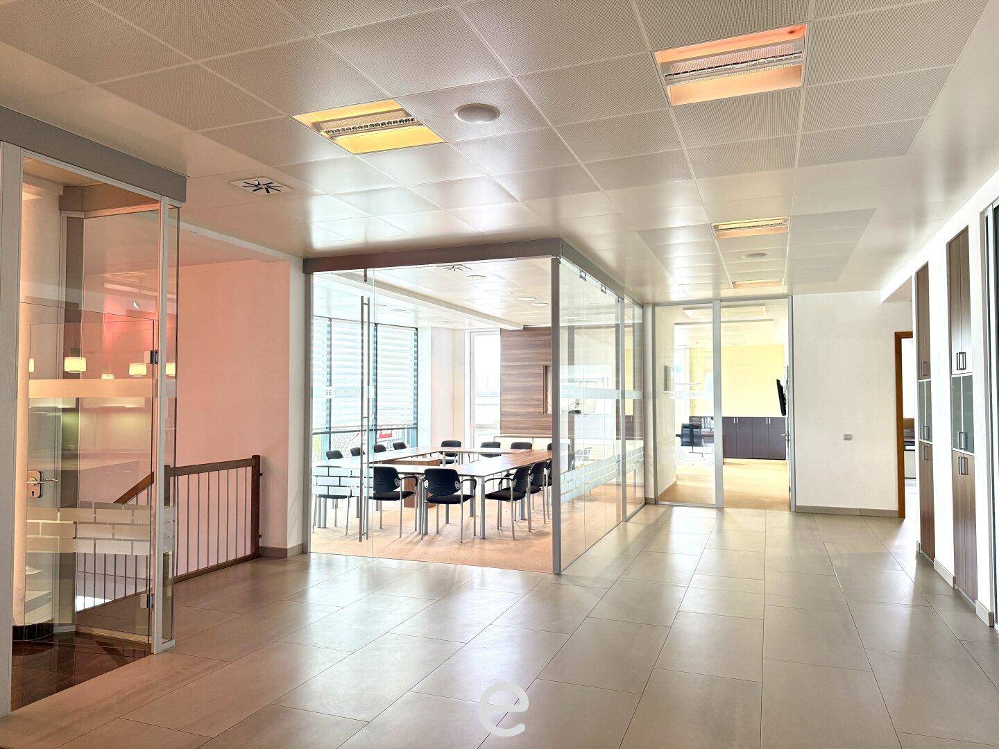 Heller Bürogang mit Glaswänden, der zu einem modernen Konferenzraum und weiteren Büros führt.