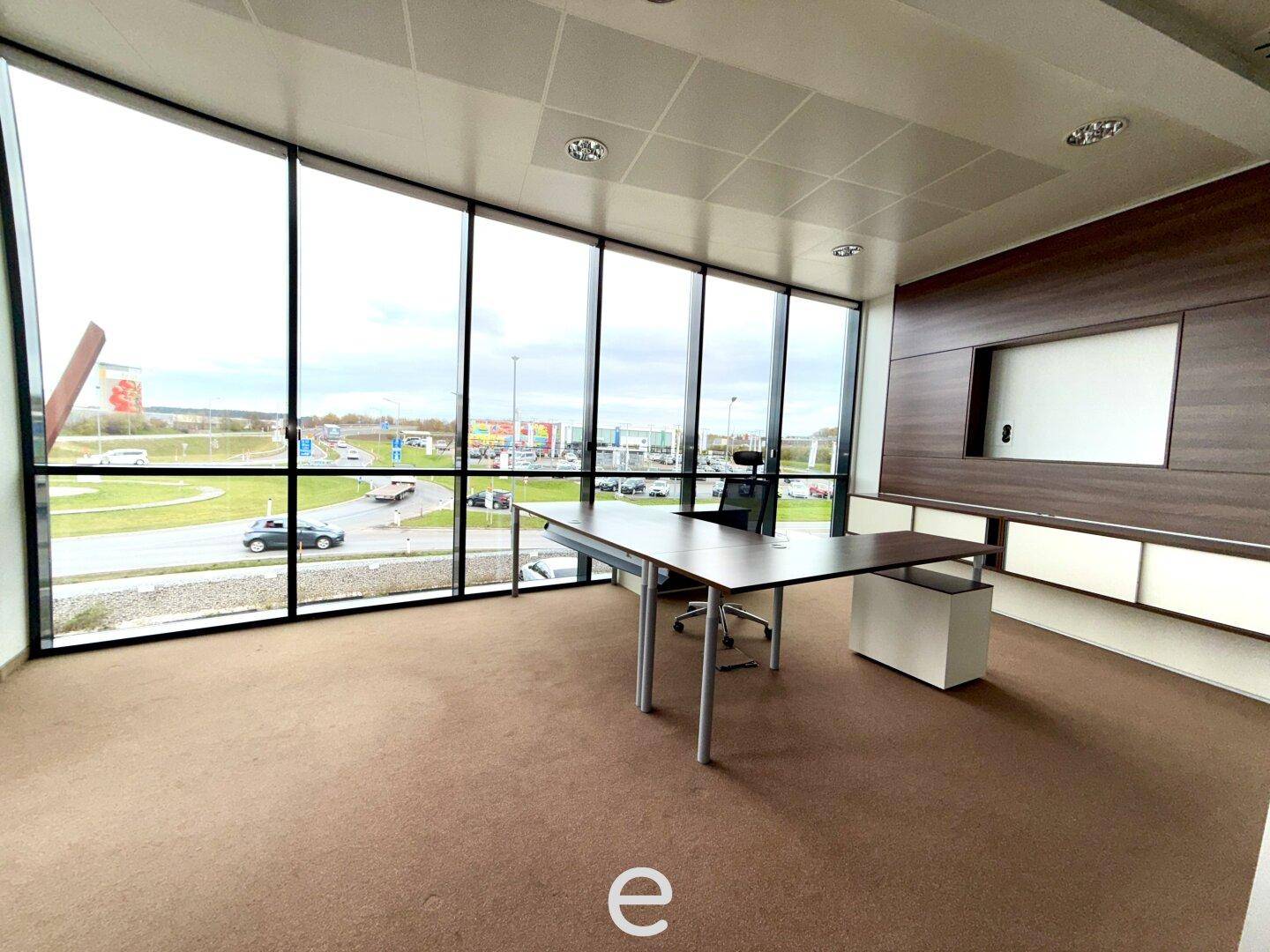 Geräumiges Büro mit Teppichboden, großen Fenstern und einem modernen Schreibtisch mit Bürostuhl.