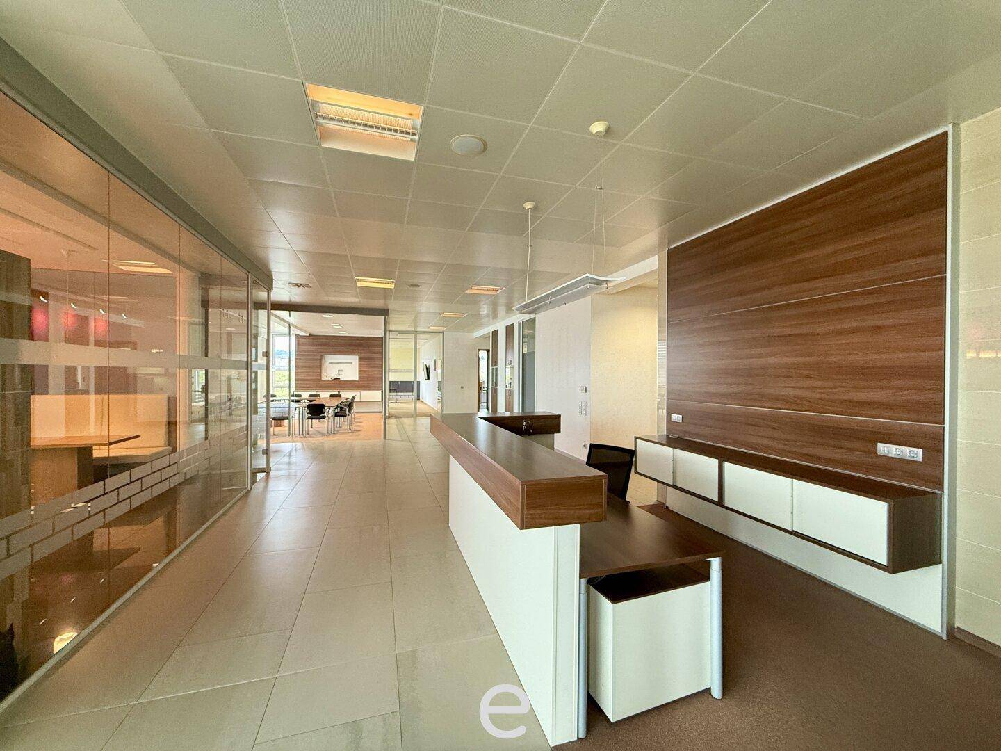 Moderner Bürogang mit Glaswänden, dunklem Fliesenboden und einer langen Holz-Empfangstheke.