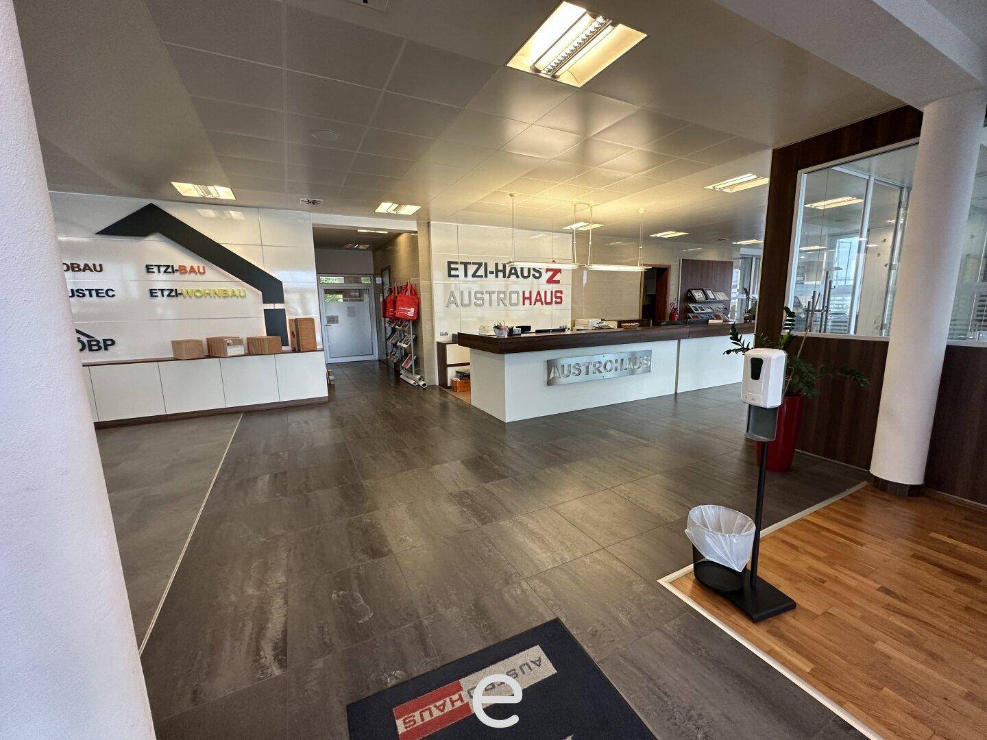 Heller Empfangsbereich mit Markenpräsentation, dunklem Fliesenboden und Holzakzenten.