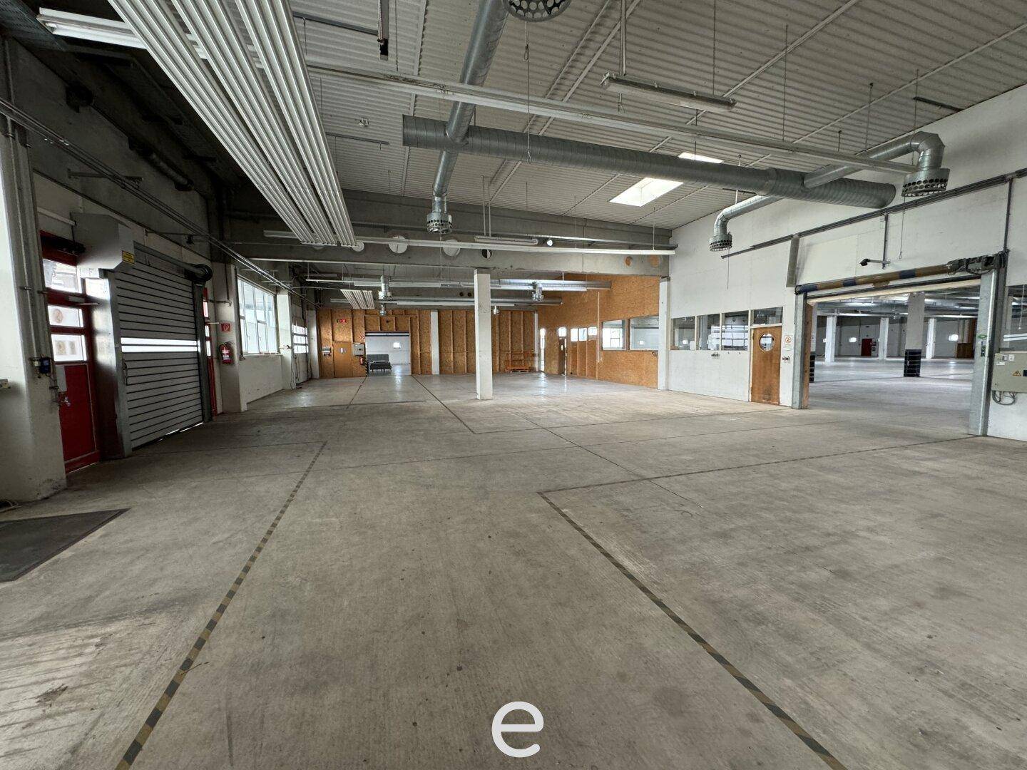 Geräumige Lagerhalle mit Rolltoren, Betonboden und sichtbaren Lüftungsanlagen unter der hohen Decke.