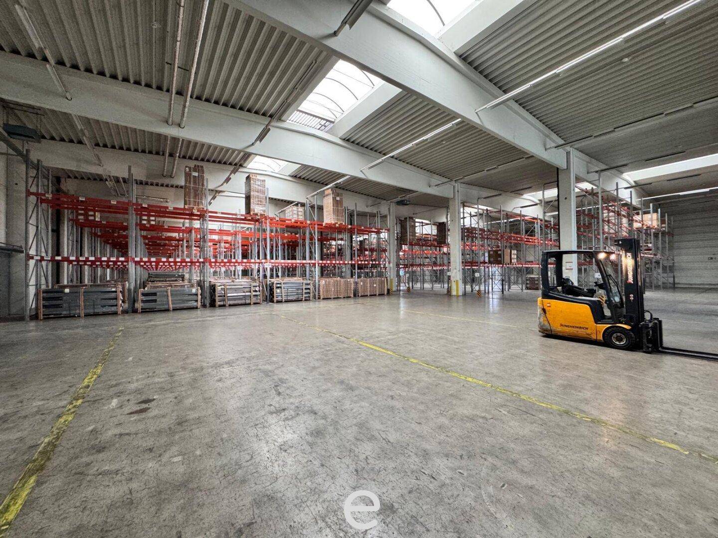 Weitläufige Lagerhalle mit Gabelstapler, hohen Regalen und natürlicher Beleuchtung durch Dachfenster.