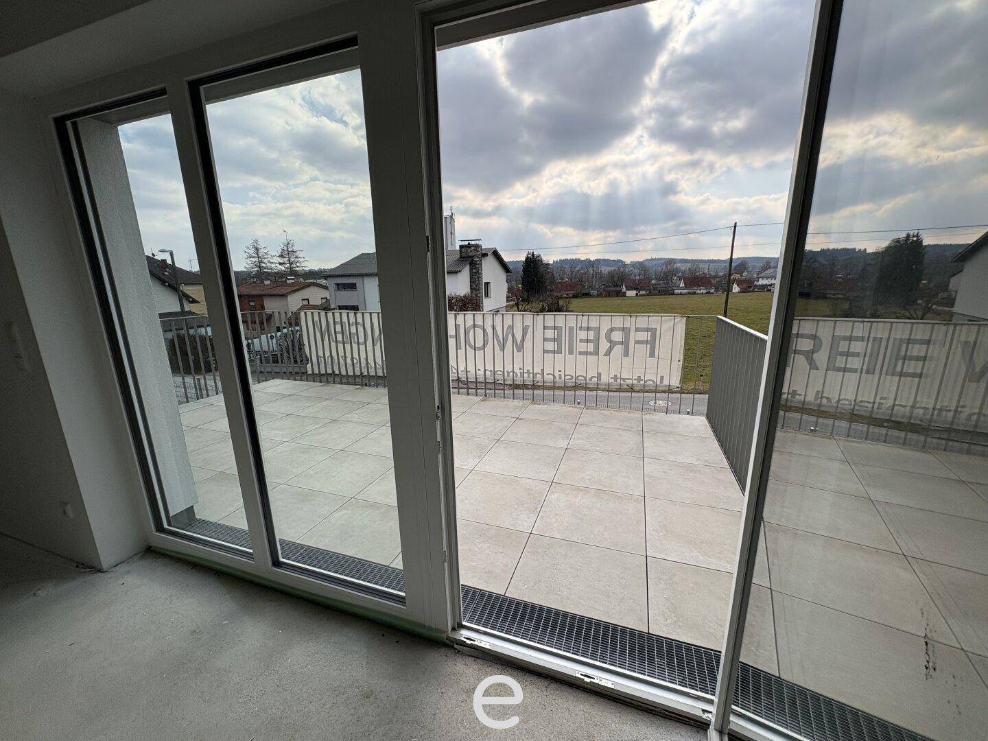 Blick vom Wohnzimmer durch große Glasfront auf die geflieste Terrasse.