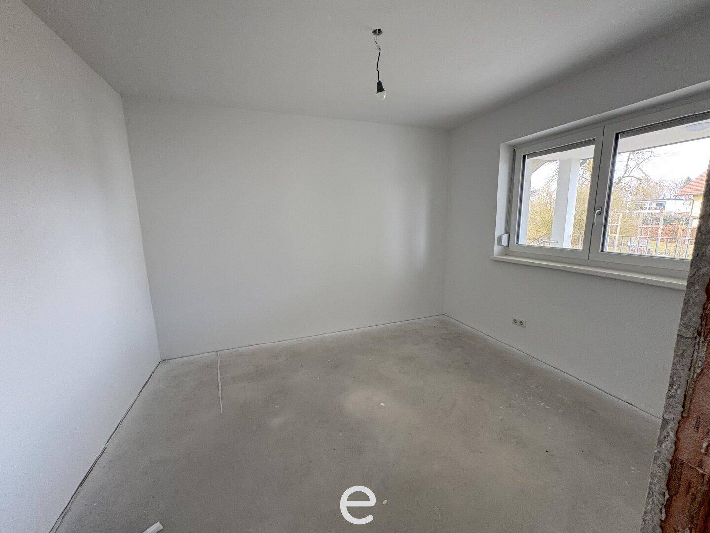 Leeres Schlafzimmer im Rohbau mit Fenster und Blick nach draußen.