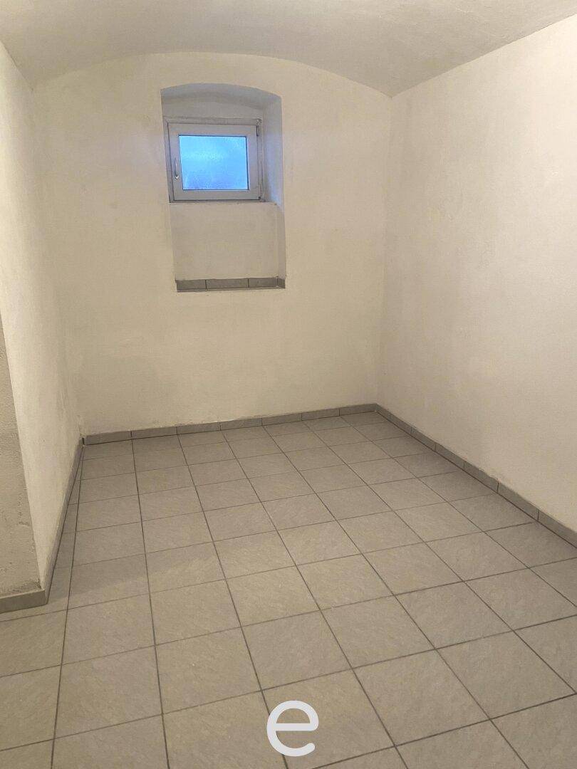 Ein leerer Kellerraum mit Fliesenboden und einem kleinen, hochgelegenen Fenster.