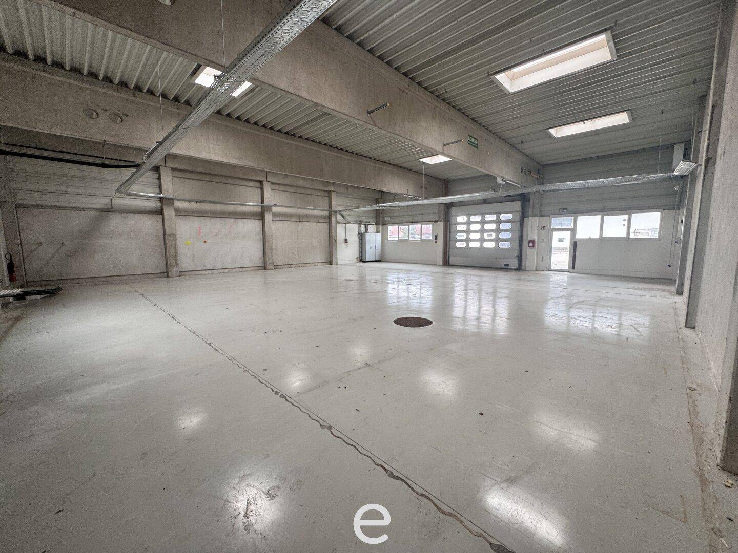 Geräumige Lagerhalle mit Betonboden, Rolltoren und Oberlichtern, ideal für gewerbliche Nutzung.