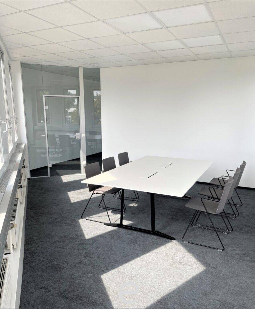 Heller Konferenzraum mit großem Tisch und bequemen Stühlen, ideal für Besprechungen und Präsentationen.