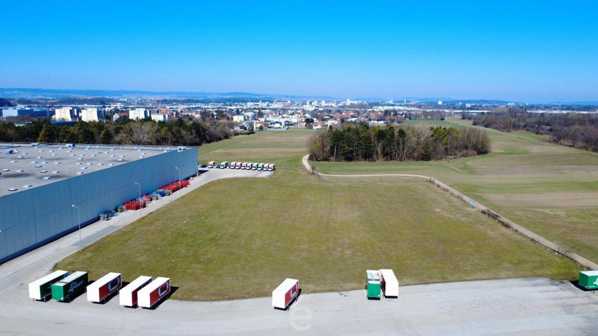 Weitläufige Grünfläche neben einem Industriegebäude, ideal für Erweiterungen oder zusätzliche Parkplätze.