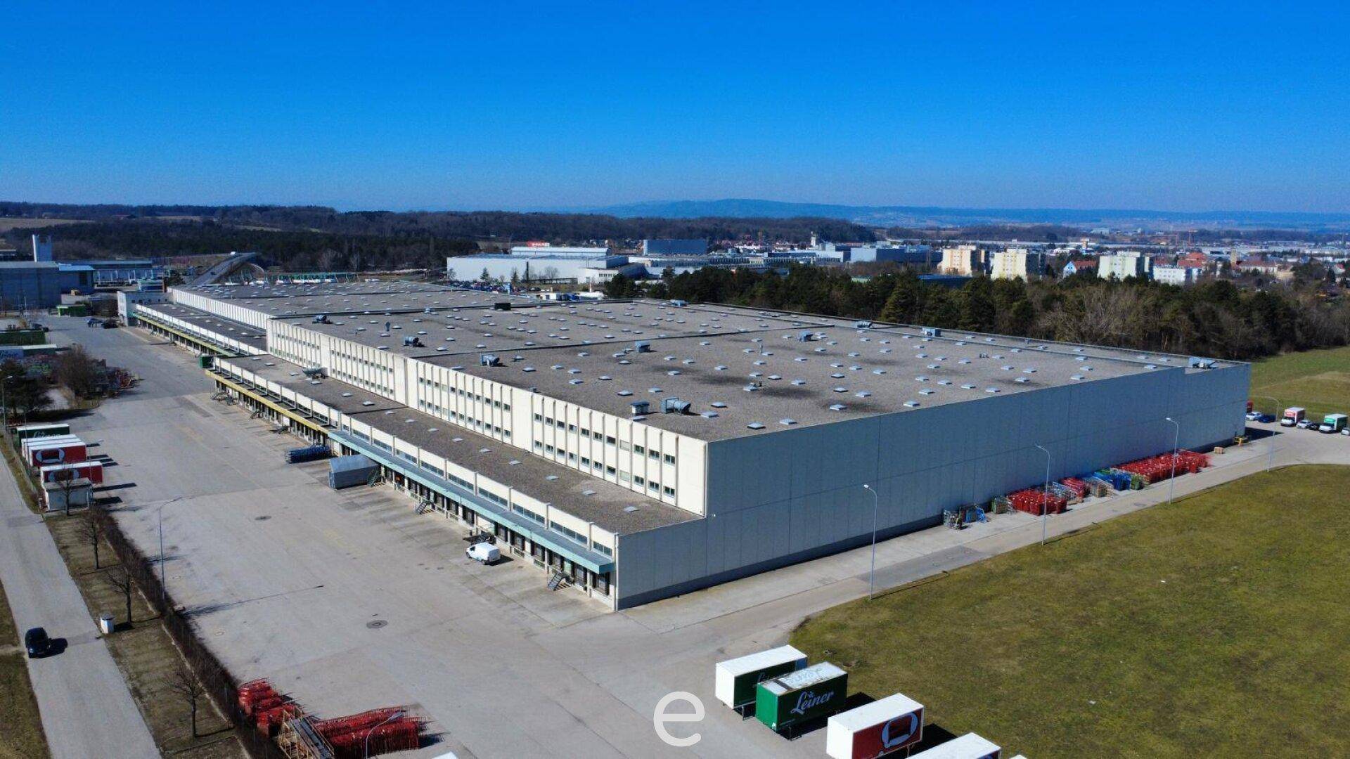 Große Logistikhalle mit zahlreichen Laderampen und weitläufigen Freiflächen für LKW-Verkehr und Lagerung.
