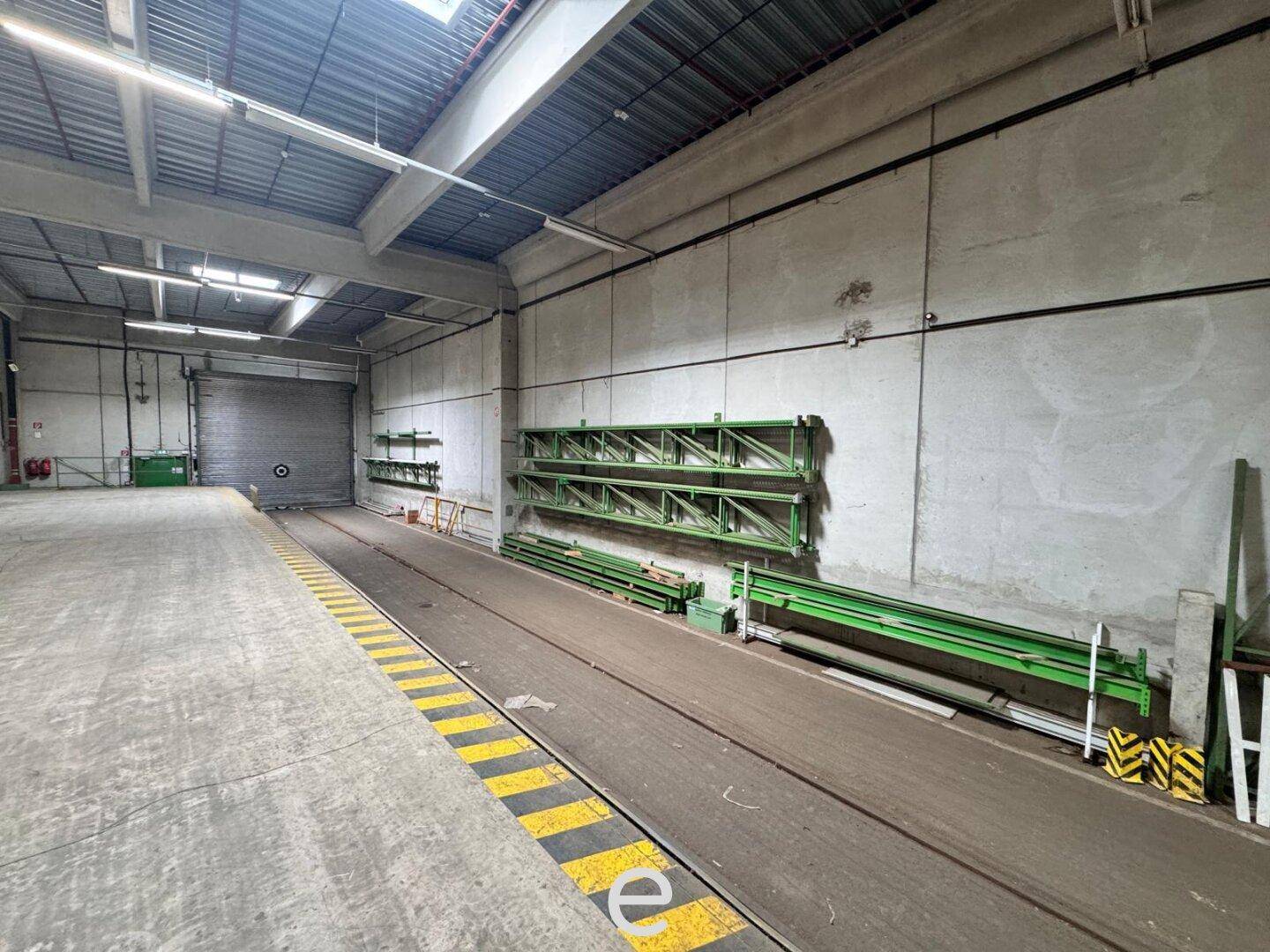 Große Lagerhalle mit Betonboden und hohen Decken, ausgestattet mit Regalsystemen und Rolltoren.