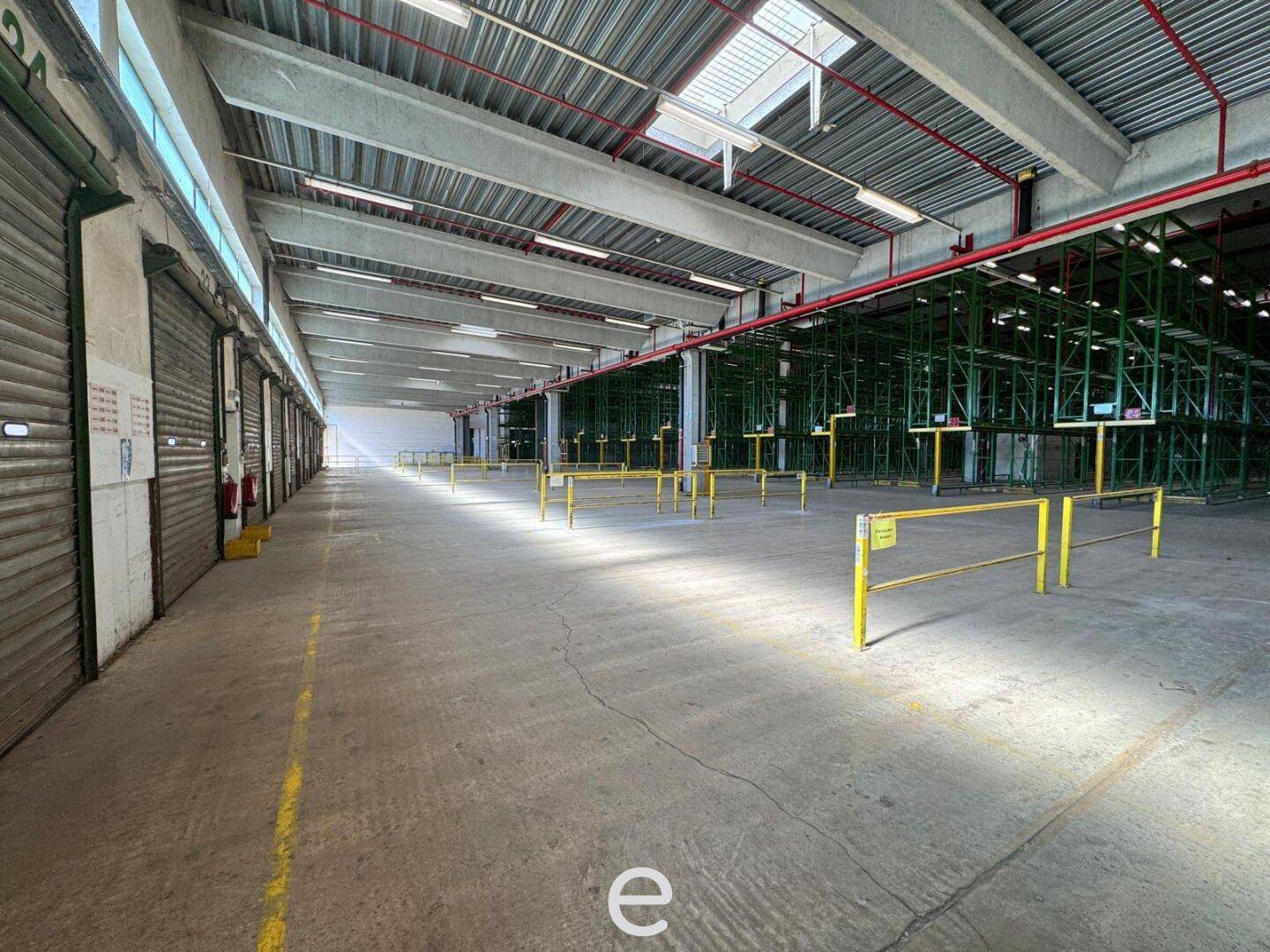 Langer Gang in einer Lagerhalle mit Rolltoren auf der linken Seite und Betonboden.