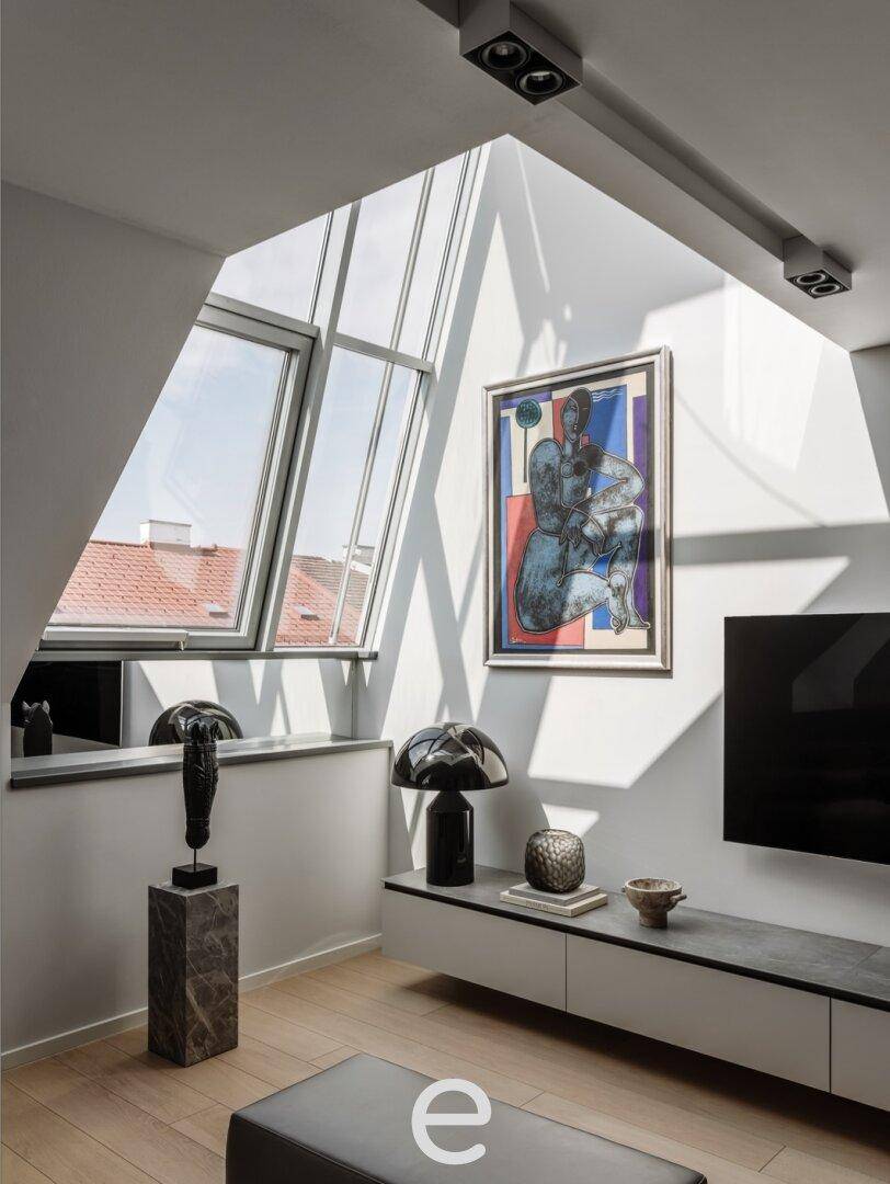 Heller Wohnbereich mit Kunstwerk, Flachbildfernseher und schrägen Dachfenstern, die Tageslicht hereinlassen.