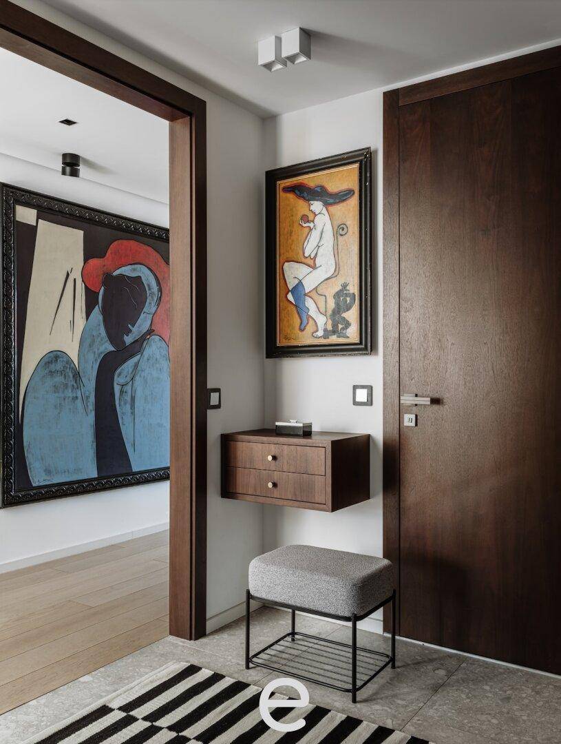 Heller Flur mit dunklen Holztüren, Kunstwerken und einem modernen Hocker, der zum Verweilen einlädt.