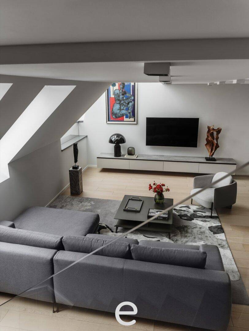 Geräumiges Wohnzimmer mit modernem Sofa, Couchtisch und Blick auf den Fernseher unter der Dachschräge.